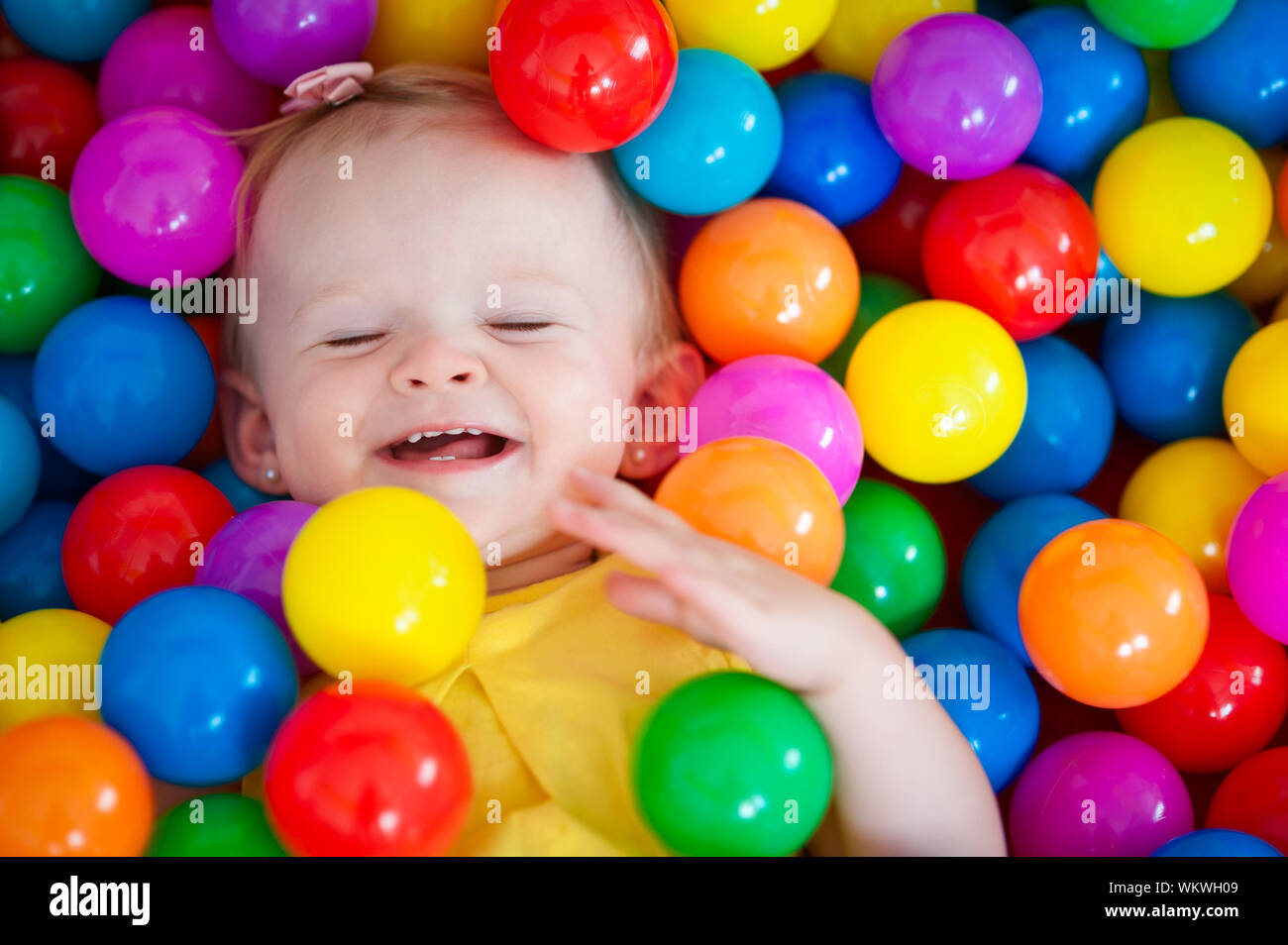 Horizontale Nahaufnahme Porträt einer 13 Monate alten Baby Mädchen spielen und lachen mit den Augen in einem bällebad Zelt zu Hause geschlossen. Stockfoto