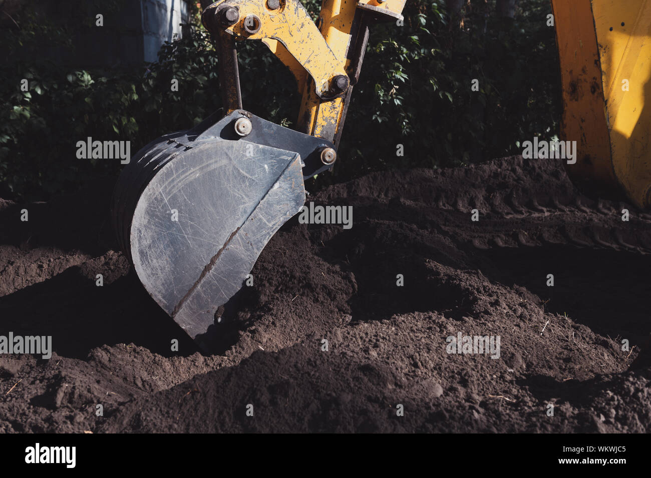 Gelber bagger Schaufel graben ein Loch in den schwarzen Boden an einem sonnigen Tag. Bau Maschinen während der Arbeit. Stockfoto