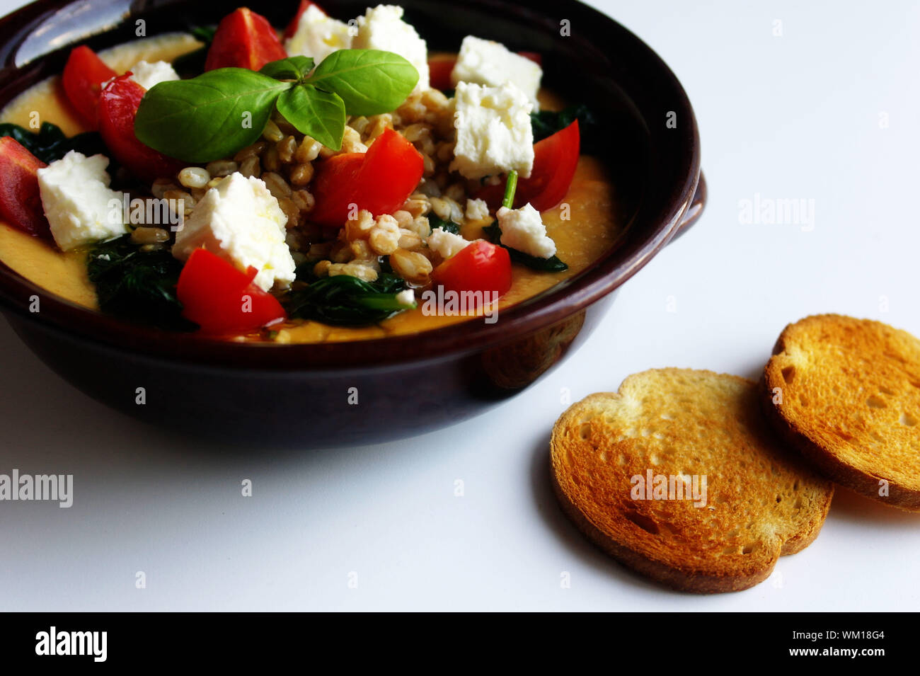 Gesunde Mahlzeiten: Gerste Suppe in einer Schüssel mit Kichererbsen, Spinat, Schafskäse, Tomaten, Basilikum und geröstetem Brot. Stockfoto