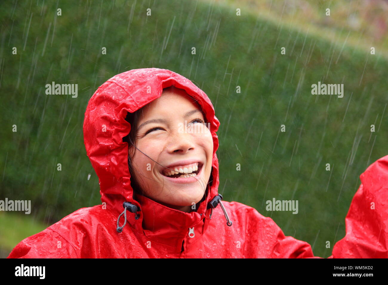 Junge Frau trägt eine rote Regenjacke genießen den Regen und Spaß außerhalb. Stockfoto