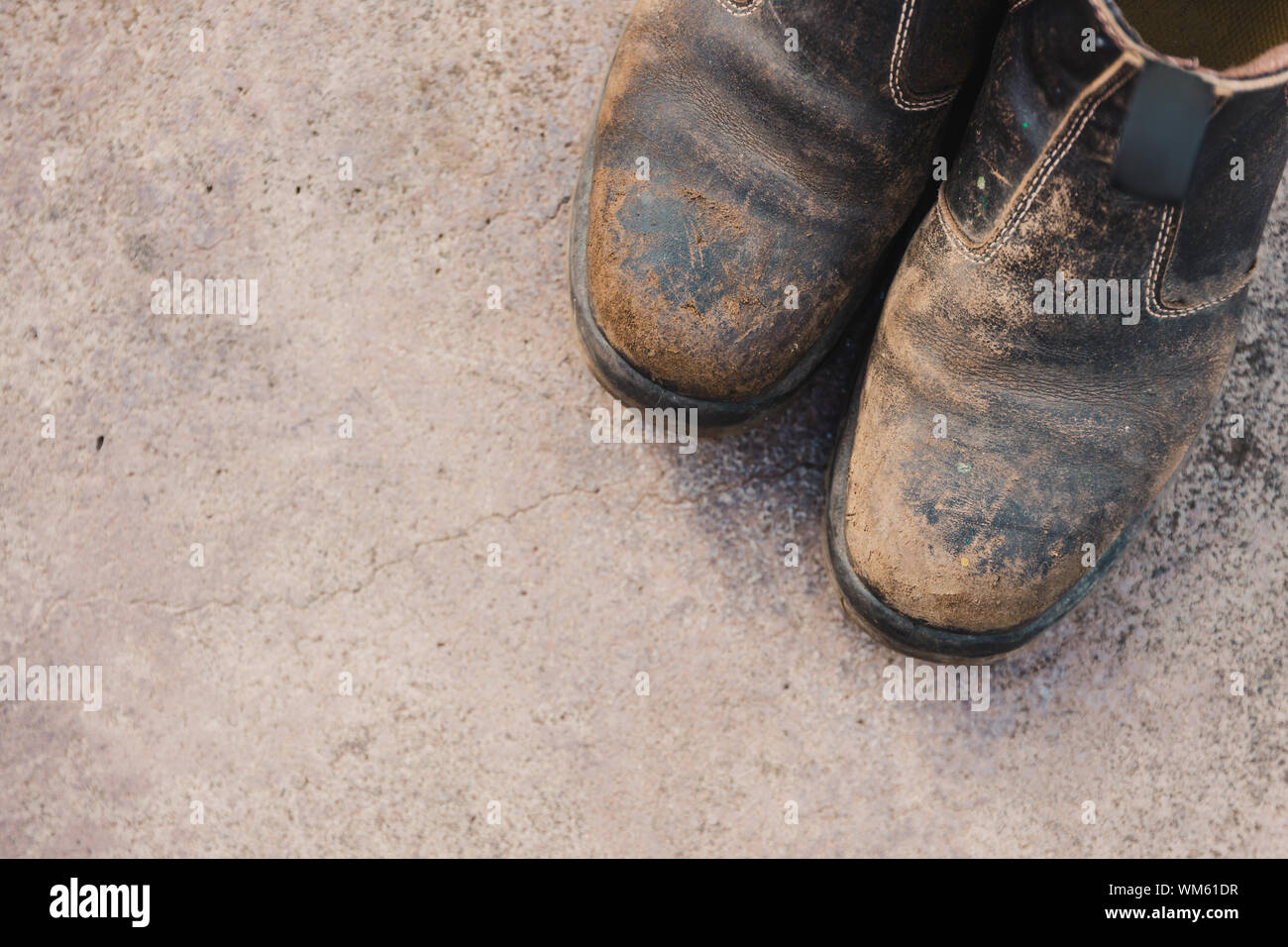 Verschlissene Schuhe auf Betonboden, Konzept der harten Arbeit in der Landwirtschaft oder in der Bauindustrie Stockfoto