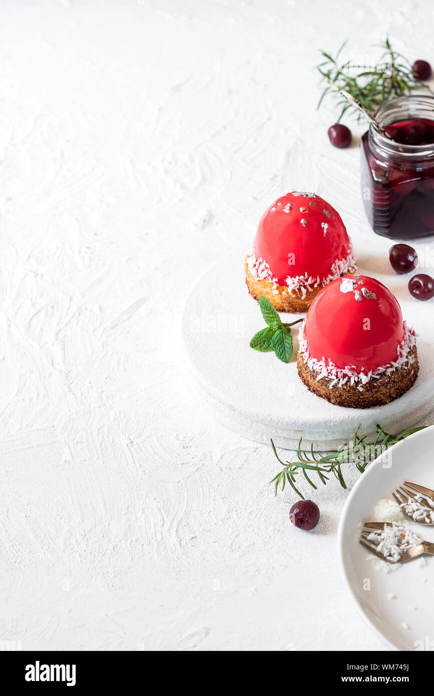 Modische Mousse Cake mit Spiegel Glasur und kirschfüllung auf ein Kissen von Kokos Plätzchen mit Kokosraspeln. Moderne Dessert. Stockfoto