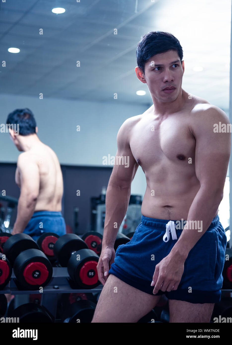 Asiatische hübscher junger muskulöser asiatischer Mann Ausübung Bodybuilder vor einem Glas im Fitnessstudio. Kerl flexing Züge seinen Bizeps Muskeln, die Karosserie an Stockfoto