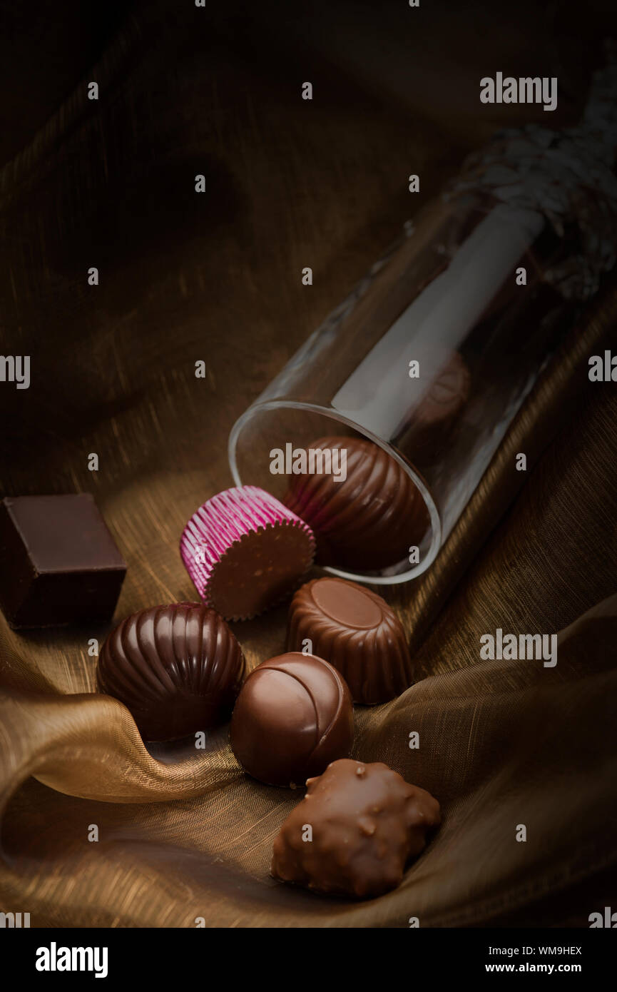 Handgefertigte edle Pralinen in verschiedenen Formen und Geschmacksrichtungen in einem Glasröhrchen Auslaufen auf weichem Stoff konzeptionelle eines romantischen Geschenk mit Copyspace Stockfoto