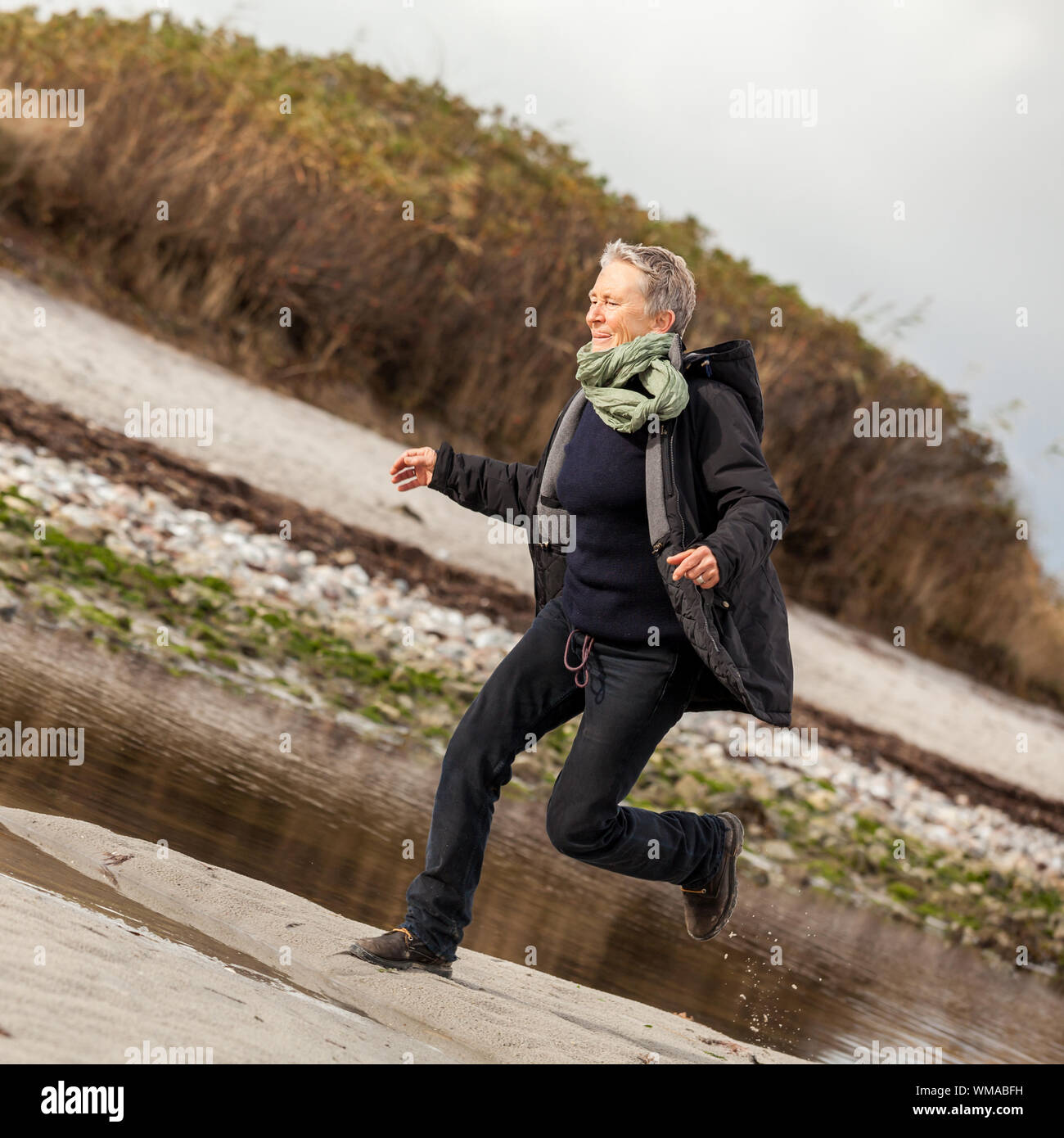 Gerne ältere Frau Herumtollen am Strand schreiten zusammen mit ausgebreiteten Armen und einem Lächeln der Anerkennung, die sie genießt die Natur und die Freiheit ihrer Stockfoto