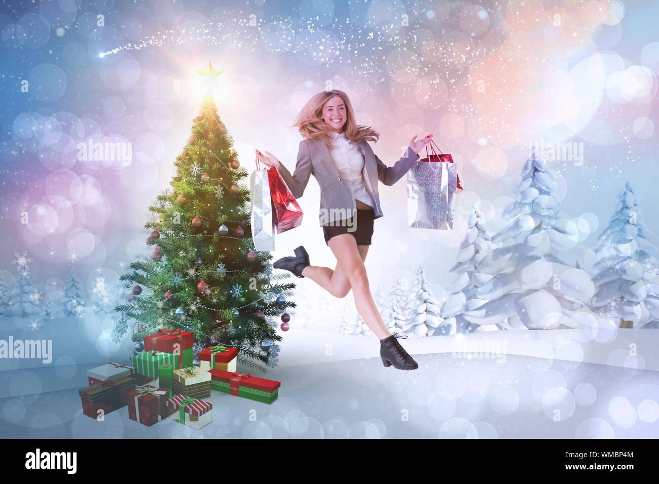 Festliche Blondine springen mit Einkaufstaschen gegen verschneite Landschaft mit Tannen Stockfoto