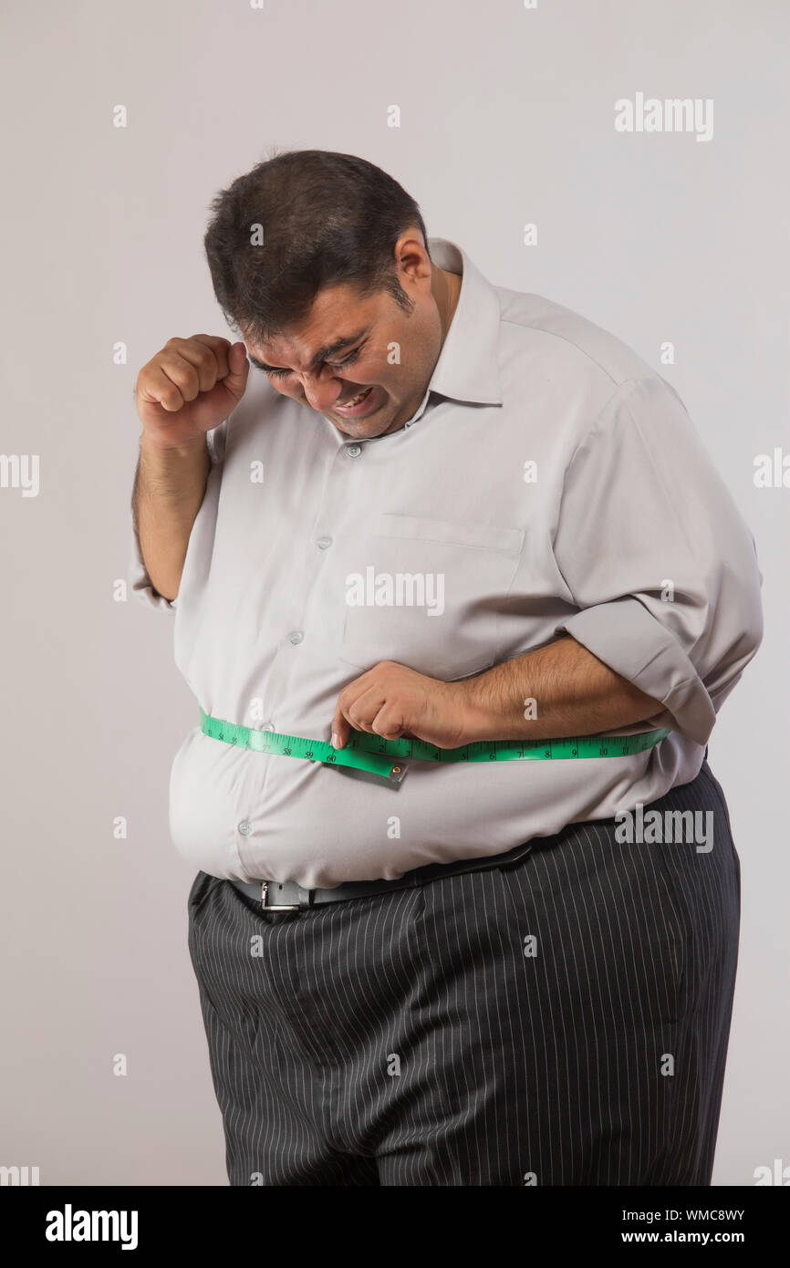 Beleibte Mann seinen Magen messen mit Maßband und Holding Faust in der Freude Stockfoto