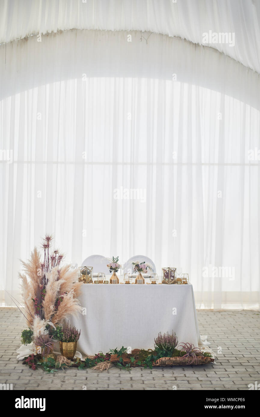 Hochzeitsdekoration im Boho-Stil.Helle Farben, im Zelt.Hochzeitstisch mit Pampas Gras verziert. Rosen und goldene geometrische Kerzenständer. Stockfoto