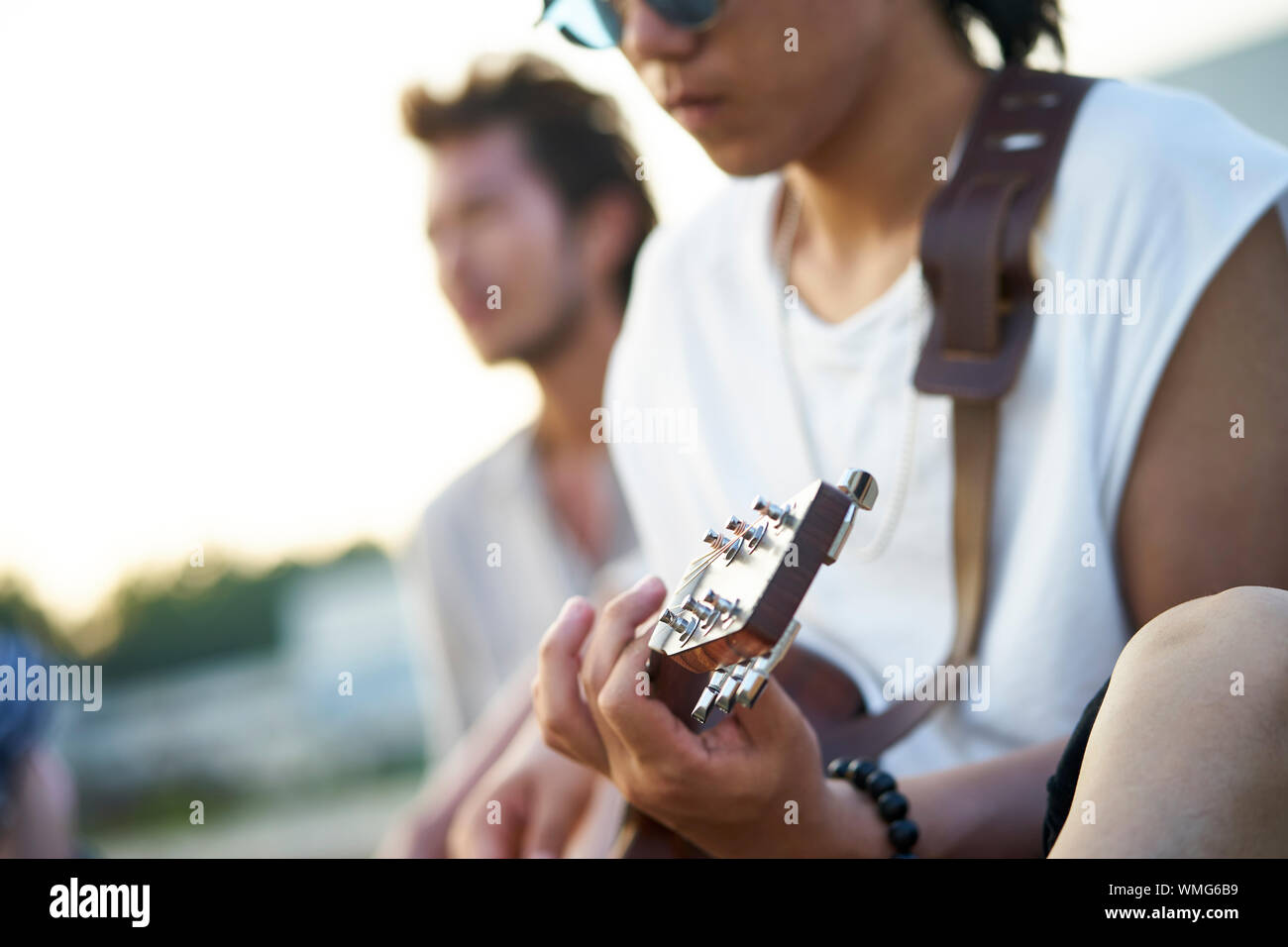 Jungen asiatischen erwachsene Männer sitzen am Strand entspannen und Gitarre spielen Stockfoto