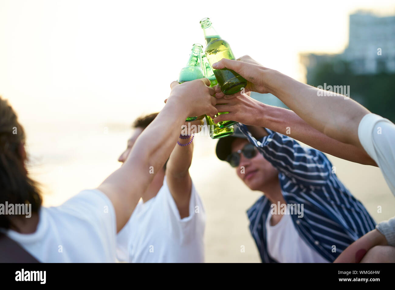 Gruppe von jungen asiatischen erwachsene Männer sitzen am Strand Toasten mit Flaschen Bier Stockfoto