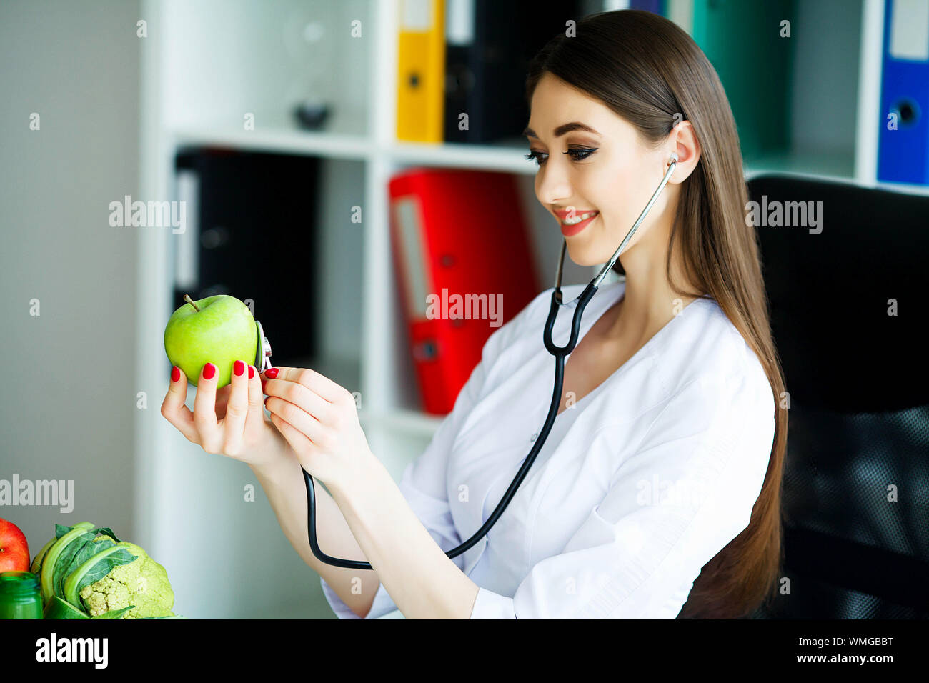 Gesundheit. Das gesunde Essen. Die Ernährungsberaterin hält in den Händen von frischen, grünen Apfel. Frisches Obst und Gemüse auf den Tisch. Gerne Arzt. Hohe Stockfoto