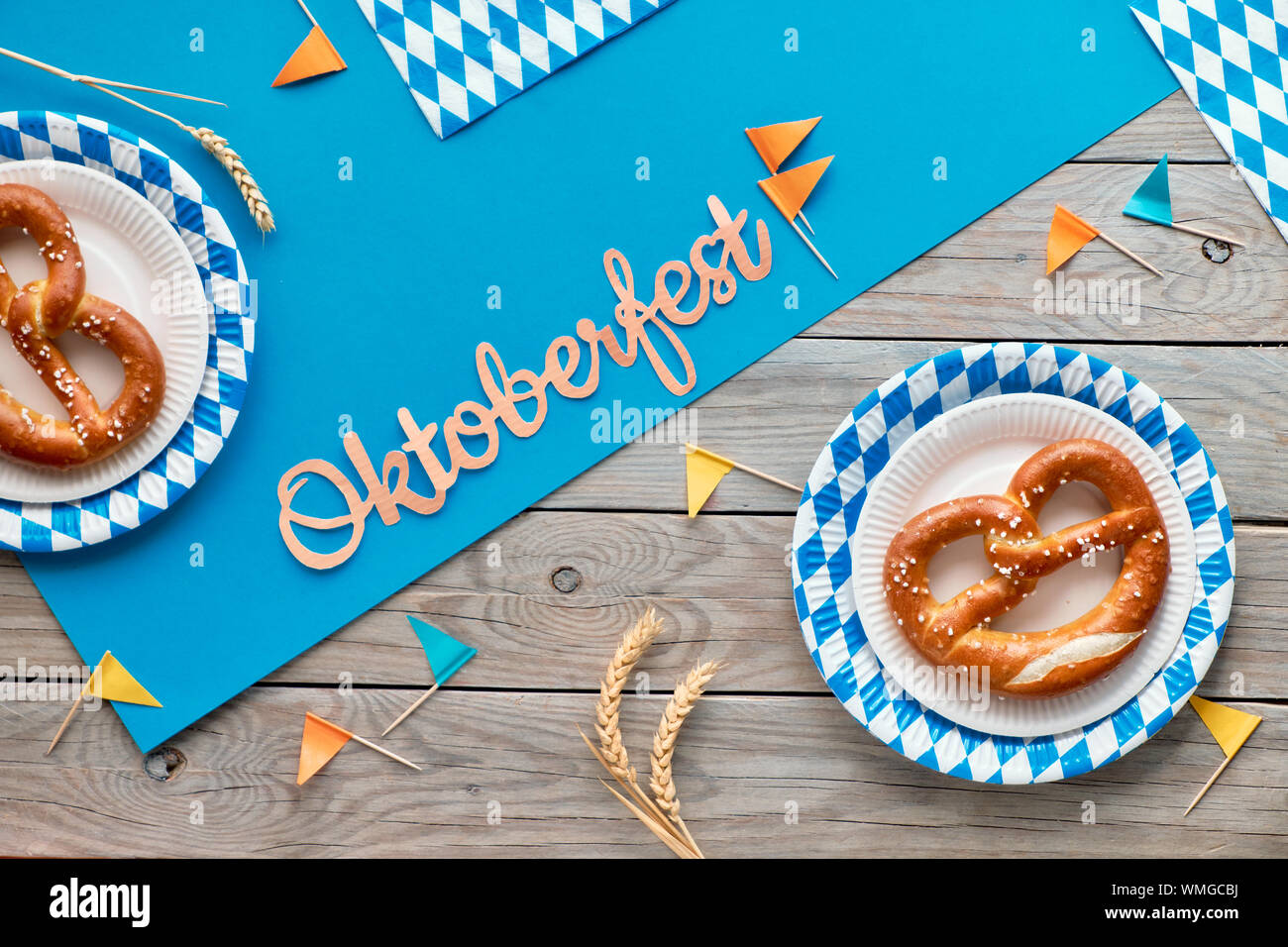 Oktoberfest, flach auf rustikalen Holztisch mit blauen Papier verteilt, Brezeln auf das verfügbare Platten, Weizenähren, dekorationsfahnen und Blätter im Herbst Stockfoto