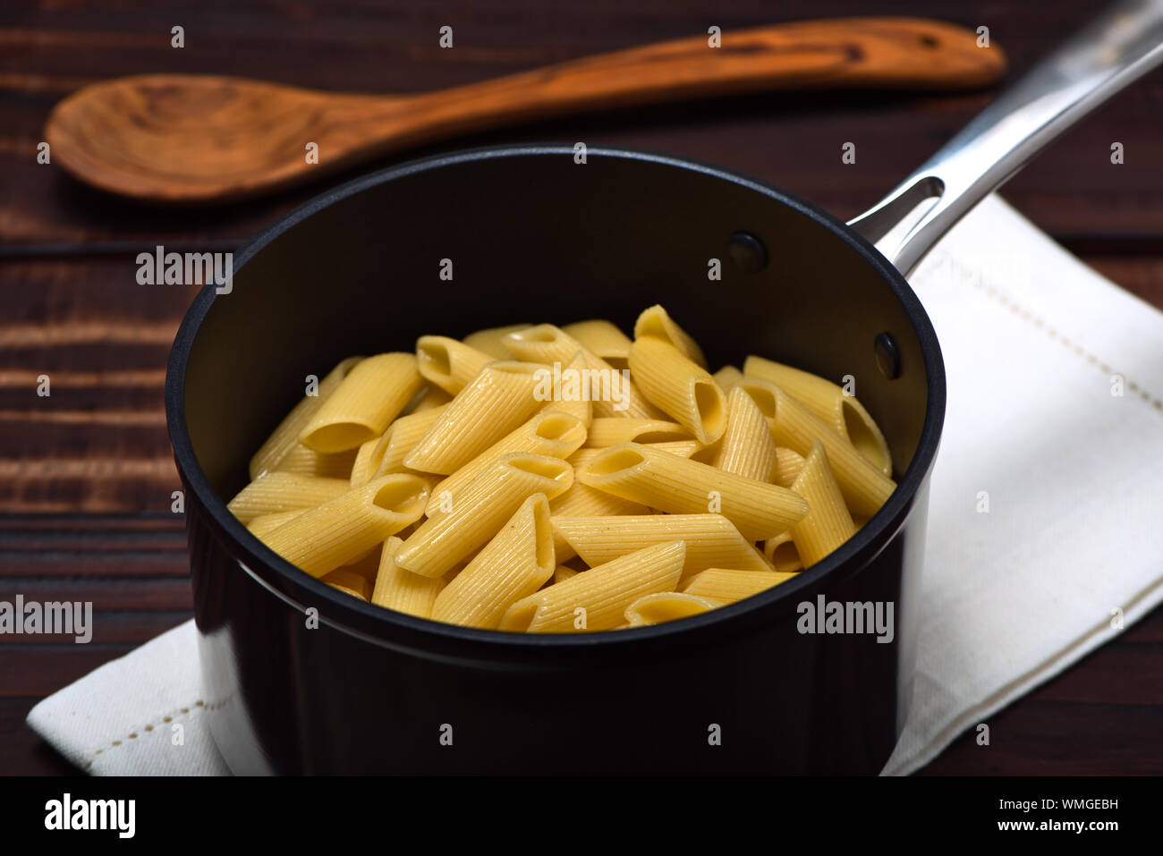 Gekochte Nudeln (Penne Rigate) in einer professionellen Eloxiert nonstick Aluminium Schwenk über eine Serviette auf einem vintage Holz- Oberfläche Stockfoto