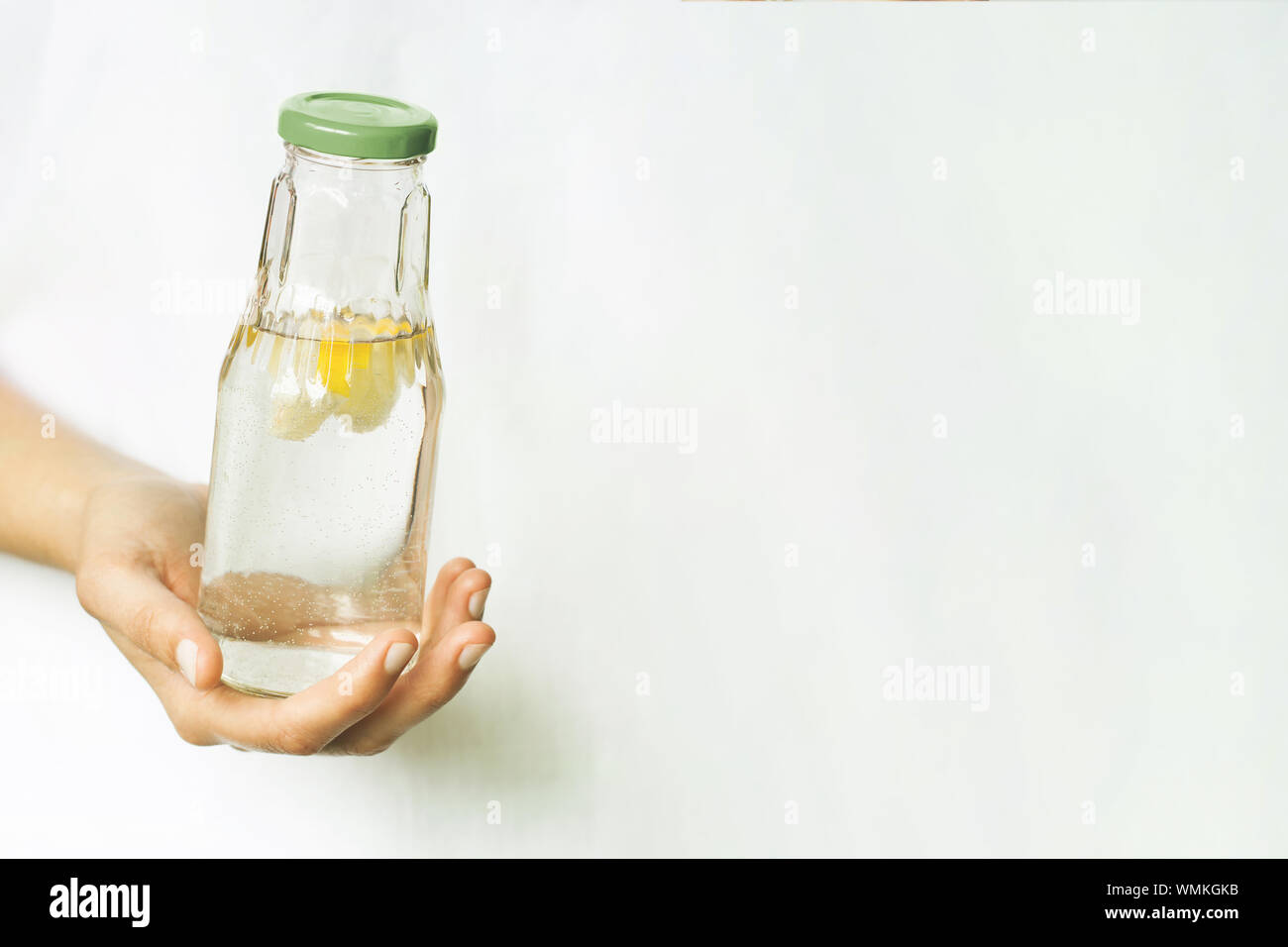 Glas Flasche mit Wasser und Zitrone in weiblicher Hand. Das Thema der Bedeutung von Trinkwasser Ihre täglichen Flüssigkeitsaufnahme. Gesunder Lebensstil, null Abfall-, Kunststoff-, Eco-friendly Shopping, vegan Stockfoto