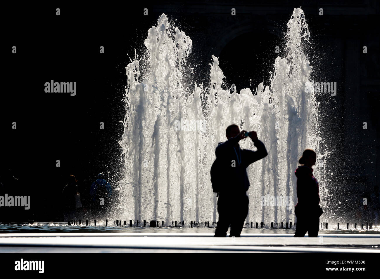 Authentische Reiseeindrücke: Touristen bilden Silhouetten gegen die Brunnen im Louvre-Hof Stockfoto