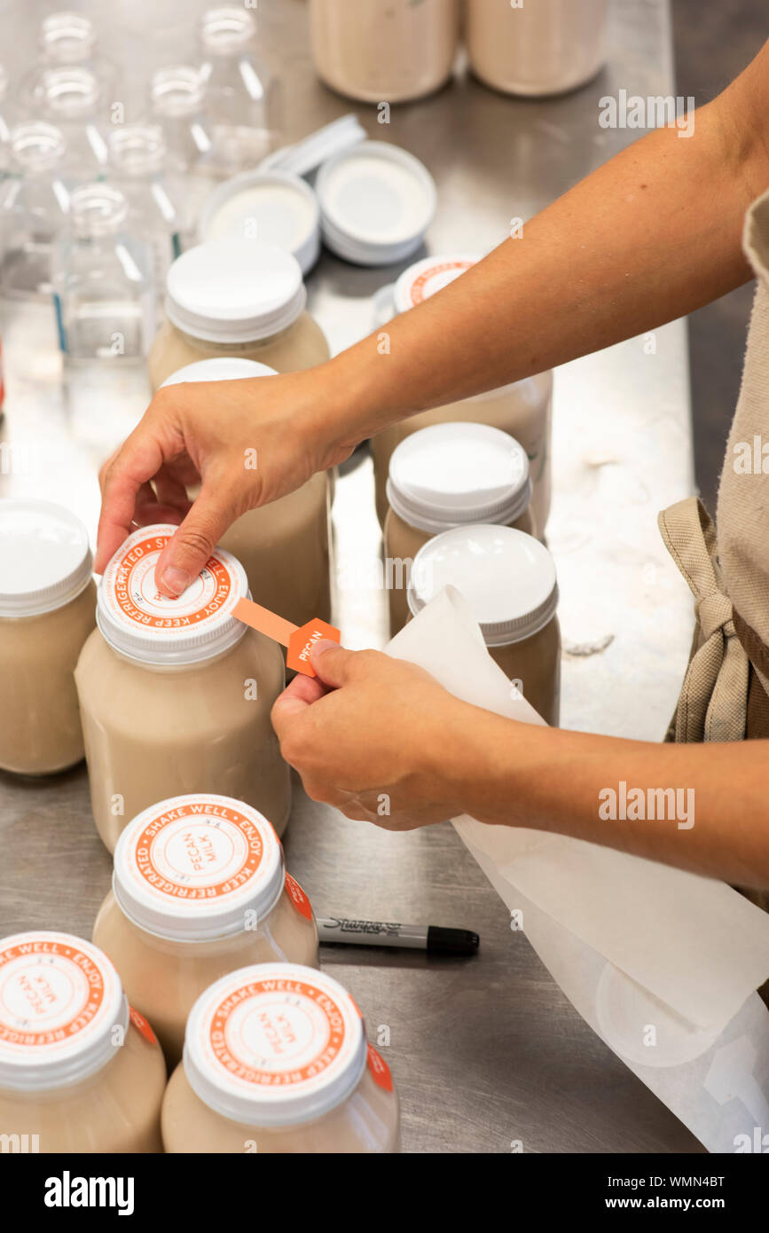 Eine Frau bringt die Etiketten auf Gläsern mit Pecan Milch Stockfoto
