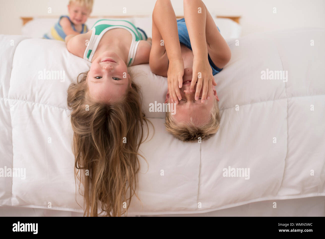 Schwester und Bruder spielen, lachen und den Kopf nach unten auf das Bett Stockfoto