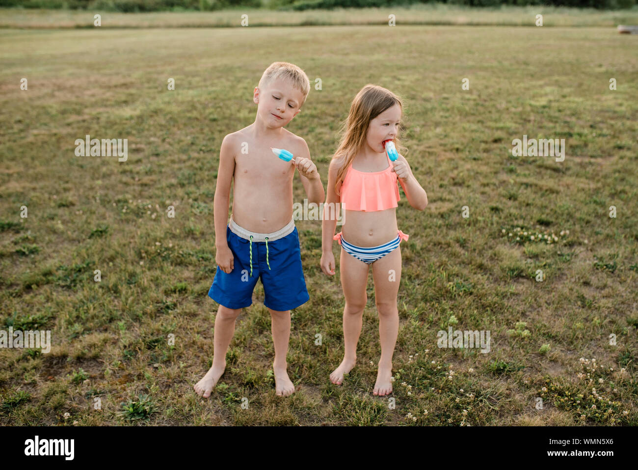 Bruder und Schwester essen Eis am Stiel das Tragen von Badeanzügen im Gras im Sommer Stockfoto