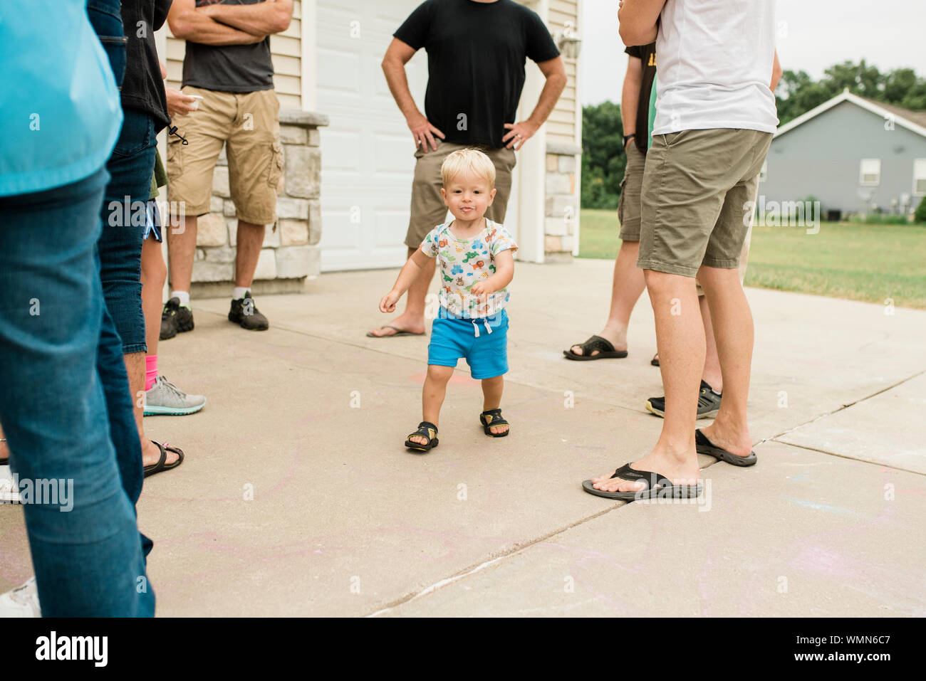 Toddler Boy mit unordentlichen Gesicht läuft durch Erwachsenen Beine in ausserhalb des Hauses Stockfoto