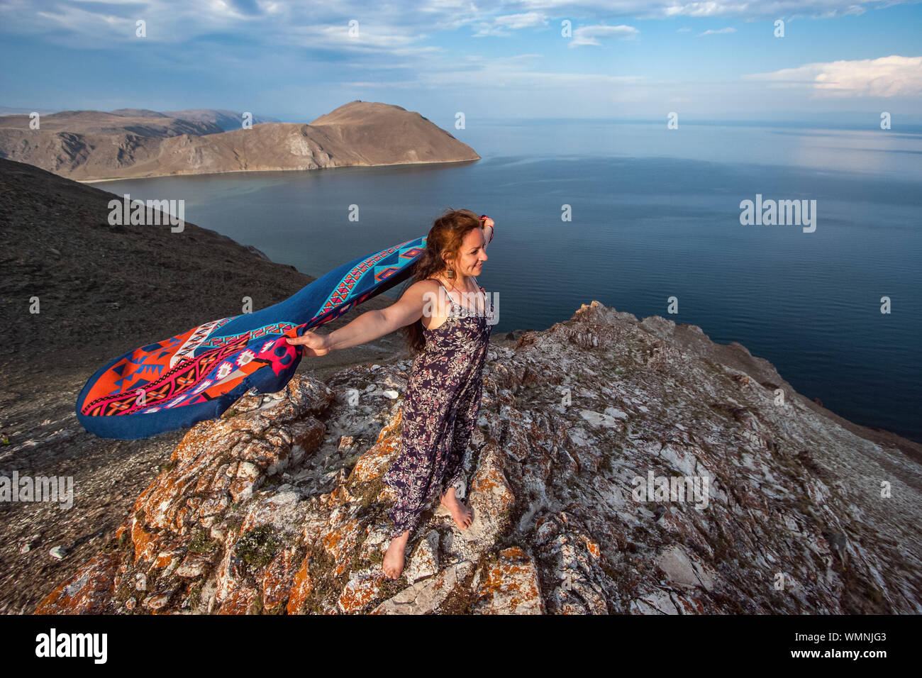 Eine nette junge Mädchen in einem Kleid mit einem bunten Schal hinter steht ein Flattern auf einem Felsen über den Baikalsee. Europäische Erscheinungsbild, lange schwarze Haare. Der Wat Stockfoto