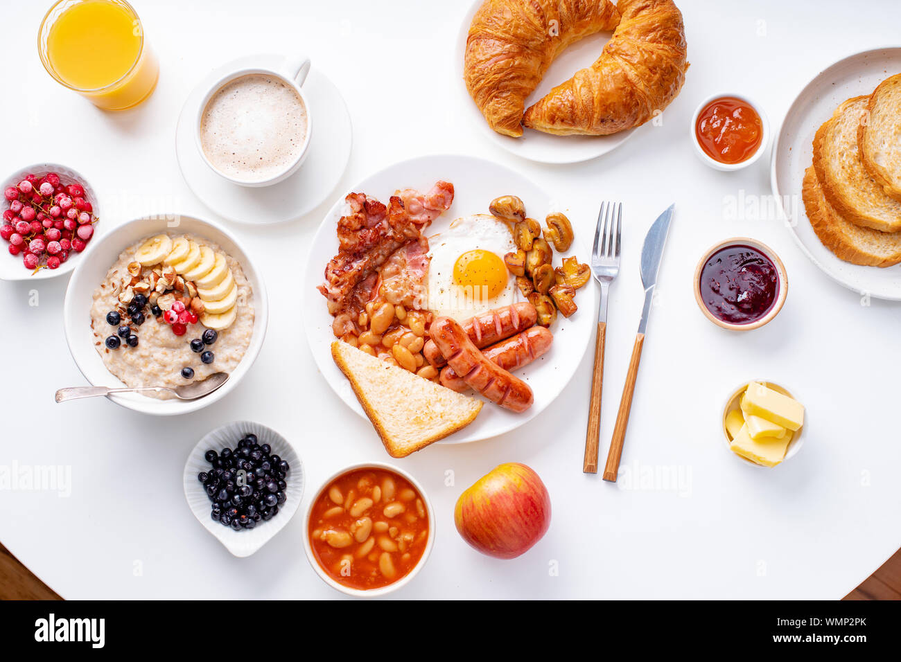 Ansicht von oben flatlay mit Sorten von frischem Frühstück: Spiegeleier mit Speck und Würstchen, Müsli mit Beeren, gebratene Toast mit Marmelade und Butter. Weiß Stockfoto