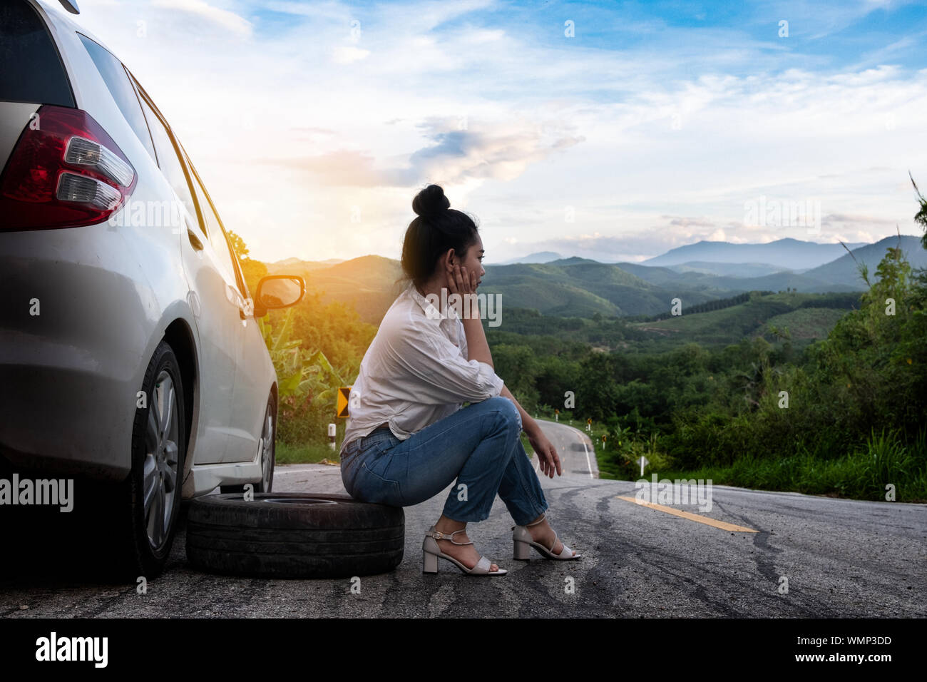 Junge hübsche Dame sitzen in der Nähe Auto für den Aufruf um Hilfe auf der öffentlichen Straße im Waldgebiet am Berg und Himmel Hintergrund Stockfoto