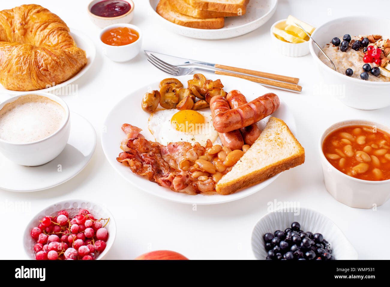 Ansicht von oben flatlay mit Sorten von frischem Frühstück: Spiegeleier mit Speck und Würstchen, Müsli mit Beeren, gebratene Toast mit Marmelade und Butter. Weiß Stockfoto