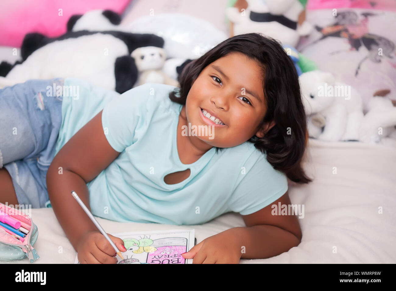 Ein Hispanic kleines Mädchen in ihrem Schlafzimmer, die glücklich Aussehen und ihre Vermehrung Hausaufgaben für eine Homeschool Curriculum. Stockfoto