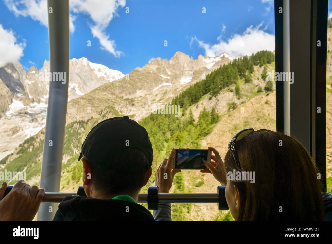 Ein Paar von hinten an Bord einer Kabine der Skyway Monte Bianco Seilbahn mit der Frau, die das Aufnehmen von Fotos mit Ihrem Smartphone, Courmayeur, Italien Stockfoto