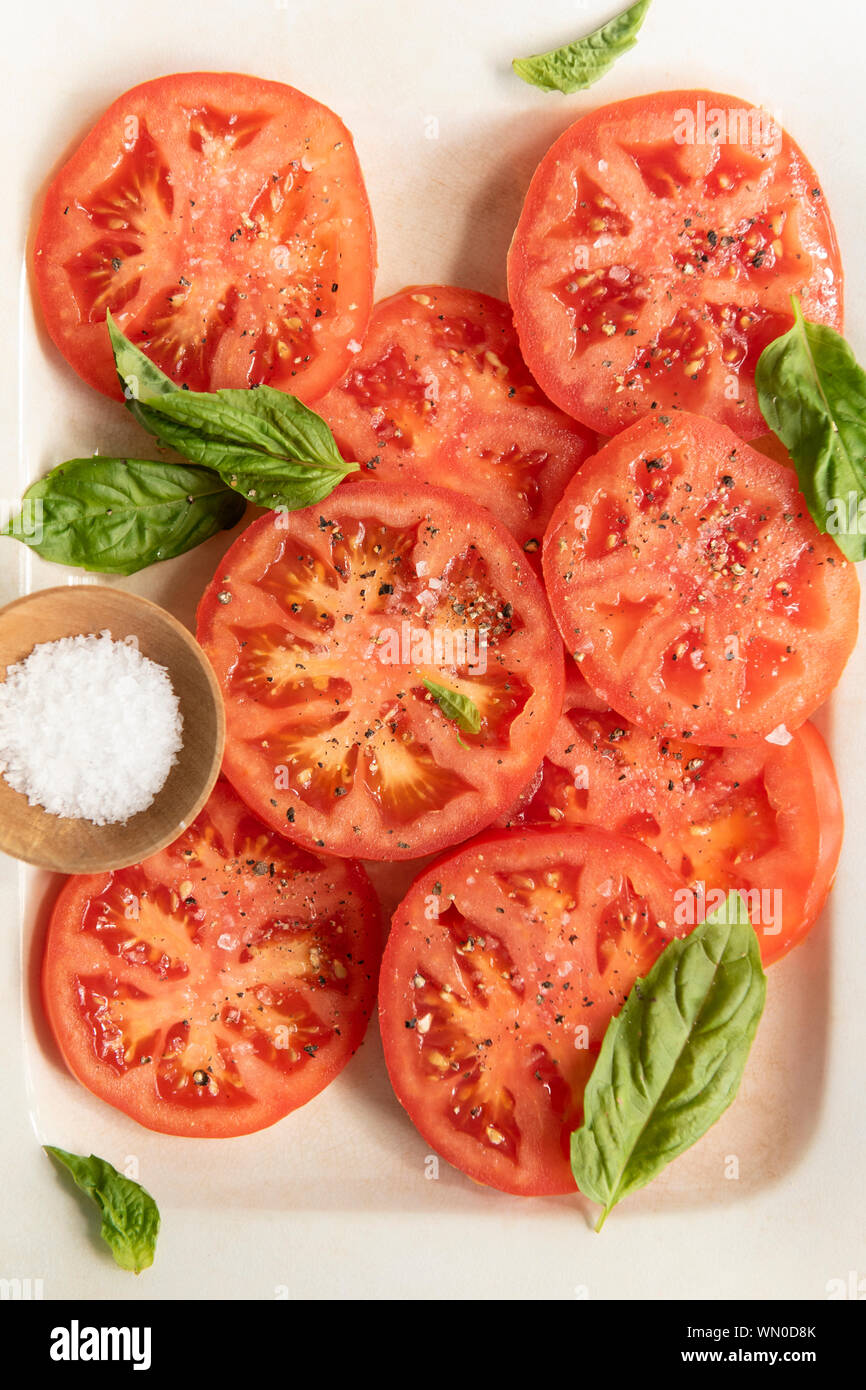 In Scheiben geschnittene Tomaten mit Basilikum und Salz Stockfoto