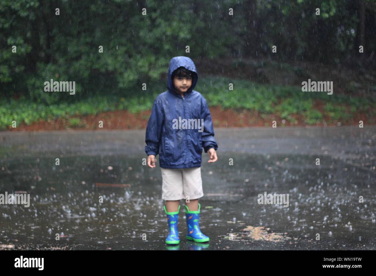 Porträt des Jungen tragen Regenjacke Steht man inmitten der Straße während der regnerischen Tag Stockfoto
