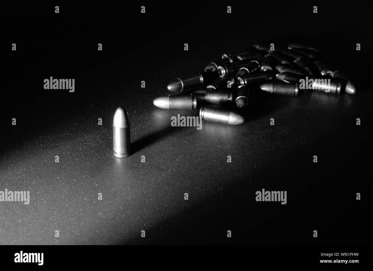 Eine einzelne 9mm bullet steht allein mit starken seitlichen Licht erzeugen lange Schatten mit einem Stapel von Kugeln im Hintergrund in Schwarz und whtie Stockfoto