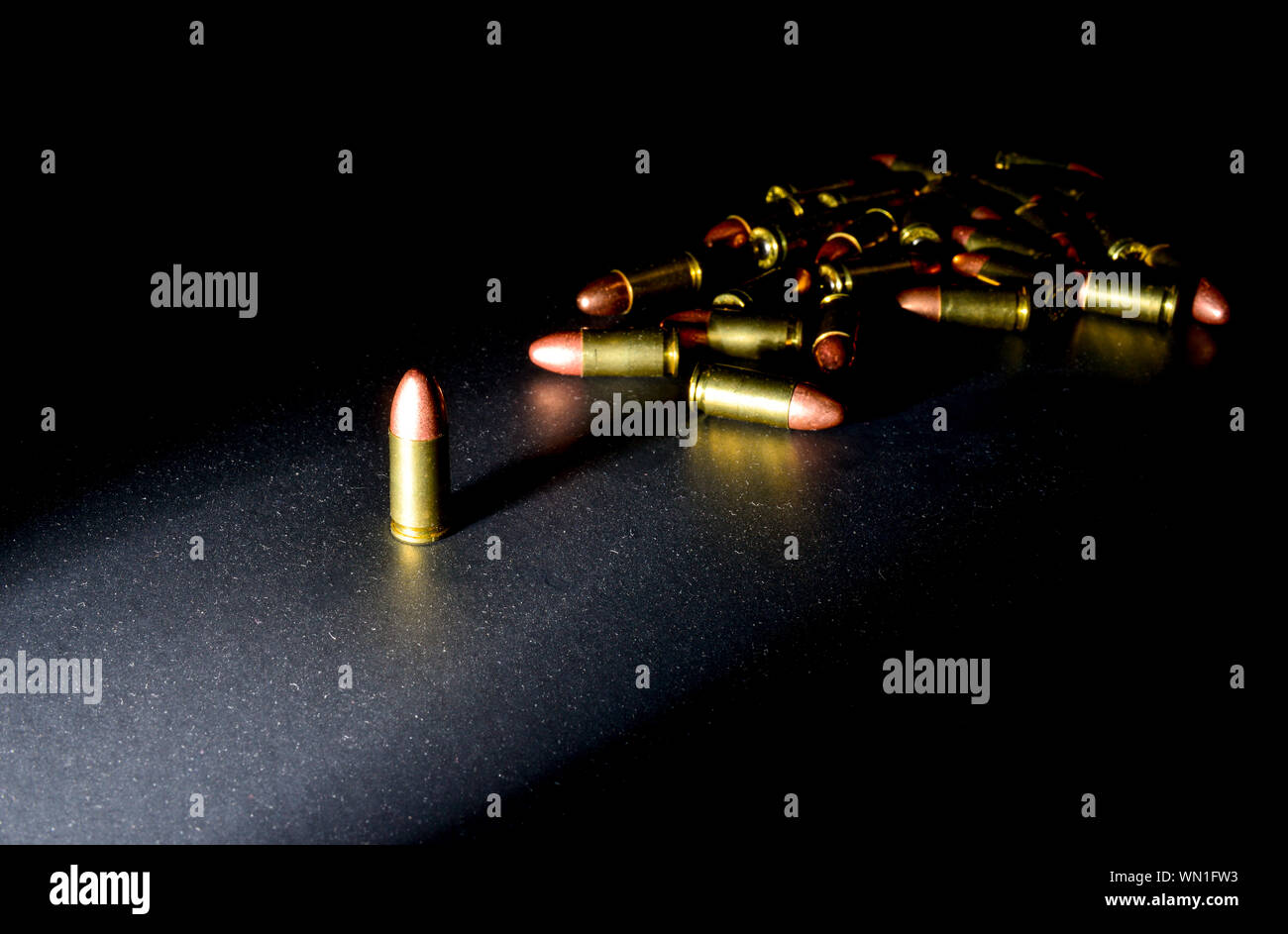 Eine einzelne 9mm bullet steht allein mit starken seitlichen Licht erzeugen intensive Farbe mit einem Stapel von Kugeln hinter im Schatten Stockfoto
