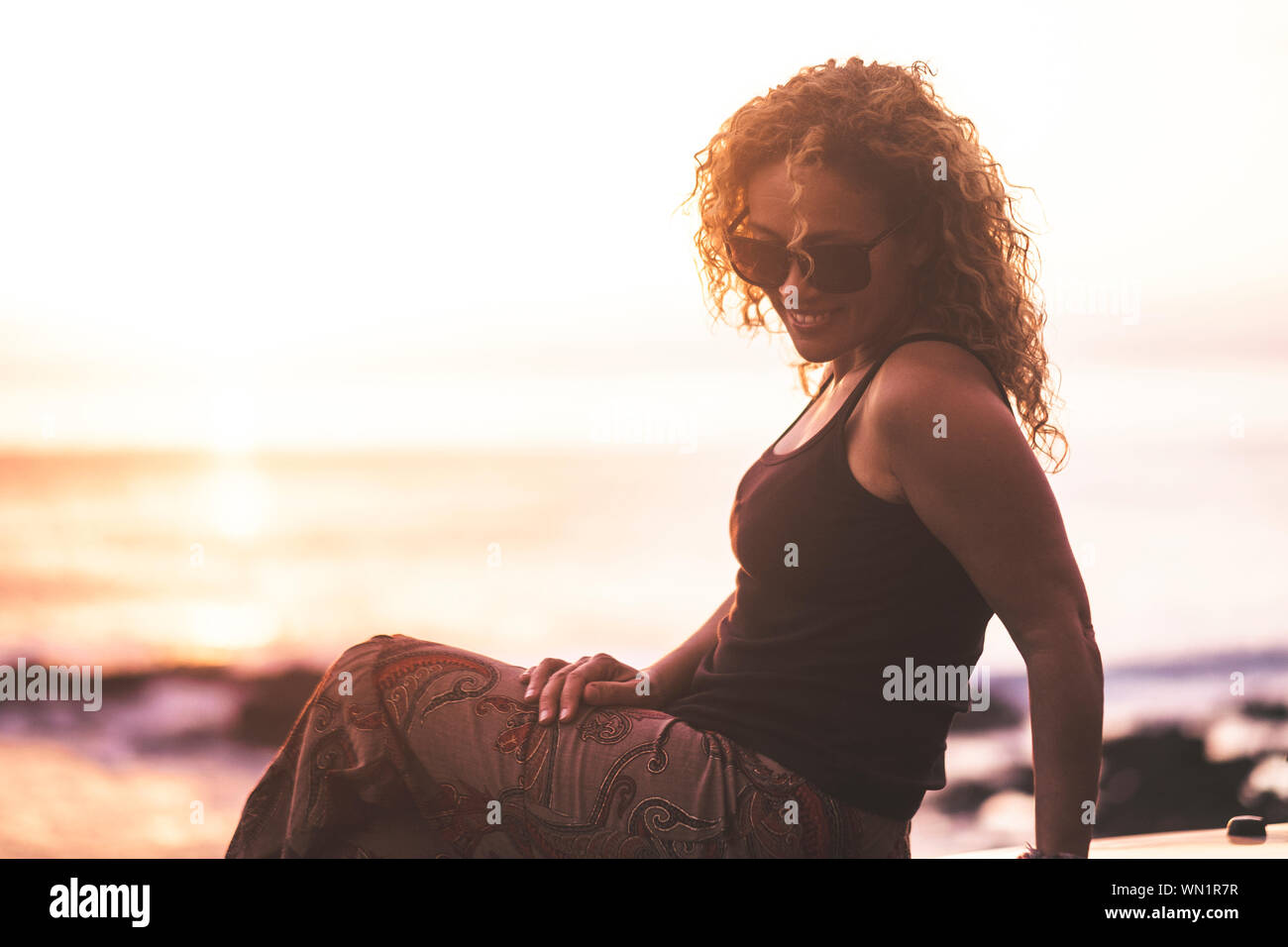 Lächelnde Frau am Strand bei Sonnenuntergang sitzen Stockfoto