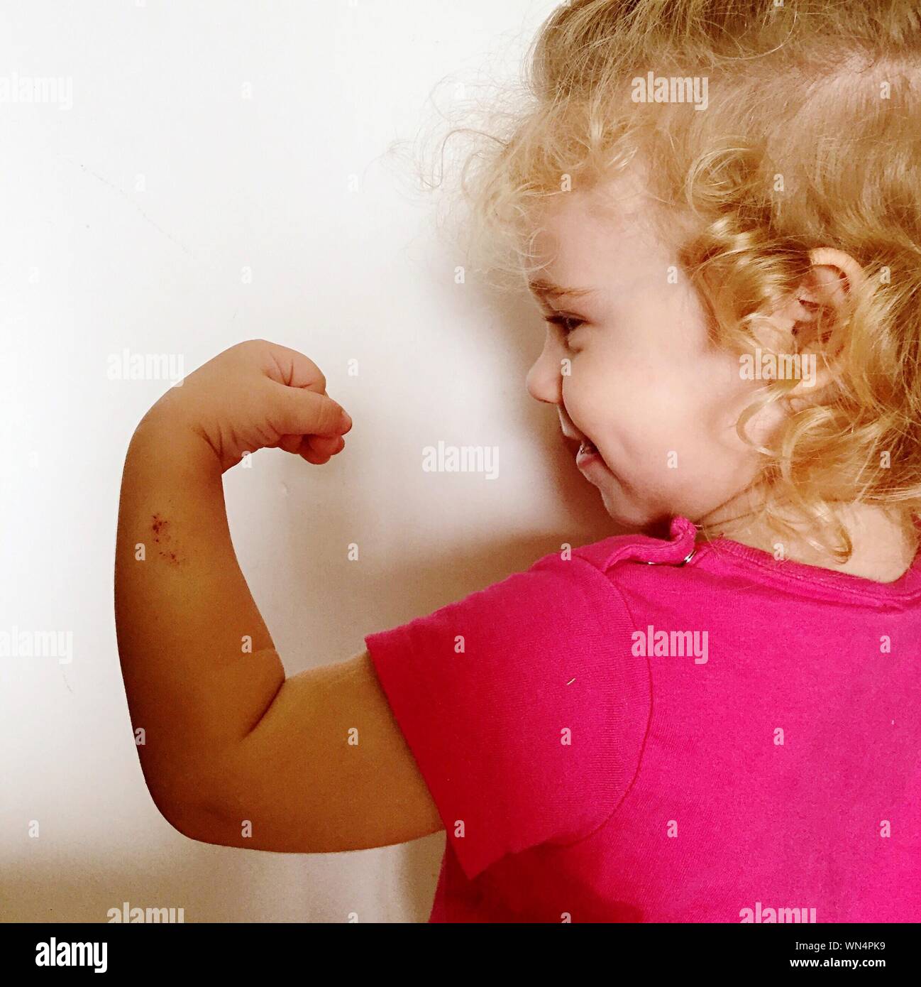 Ansicht der Rückseite des netten Mädchens Flexing Muscle gegen Weiße Wand Stockfoto