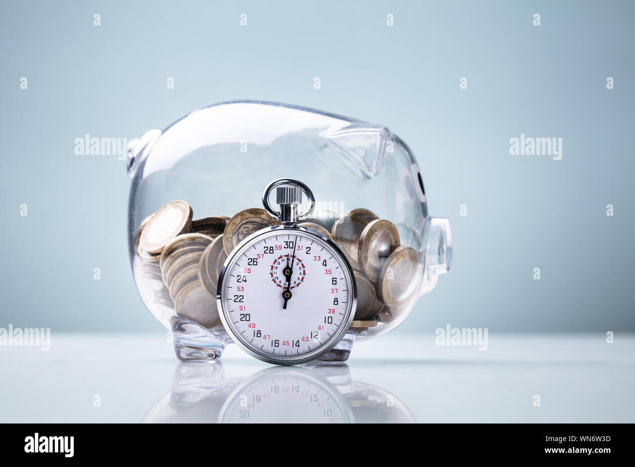 Stoppuhr lehnte sich auf transparente Sparschwein vor blauem Hintergrund Stockfoto