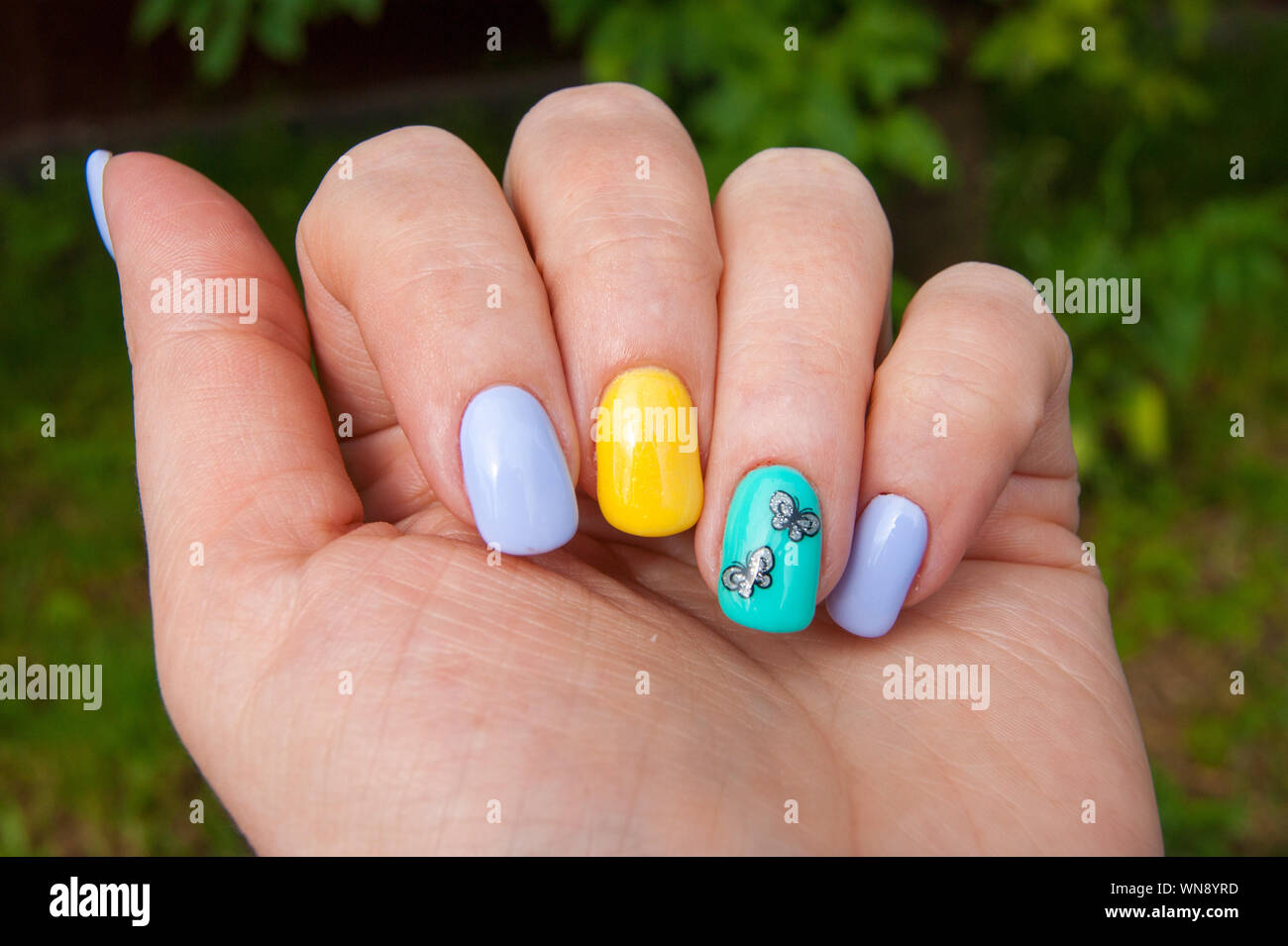 Maniküre - Gel polish Farbe in hellen Sommer Töne, Schmetterlinge sind auf einen Nagel eingefügt - Foto. Schellack, Nägel, Hände. Gesichtspflege, Glamour Stockfoto
