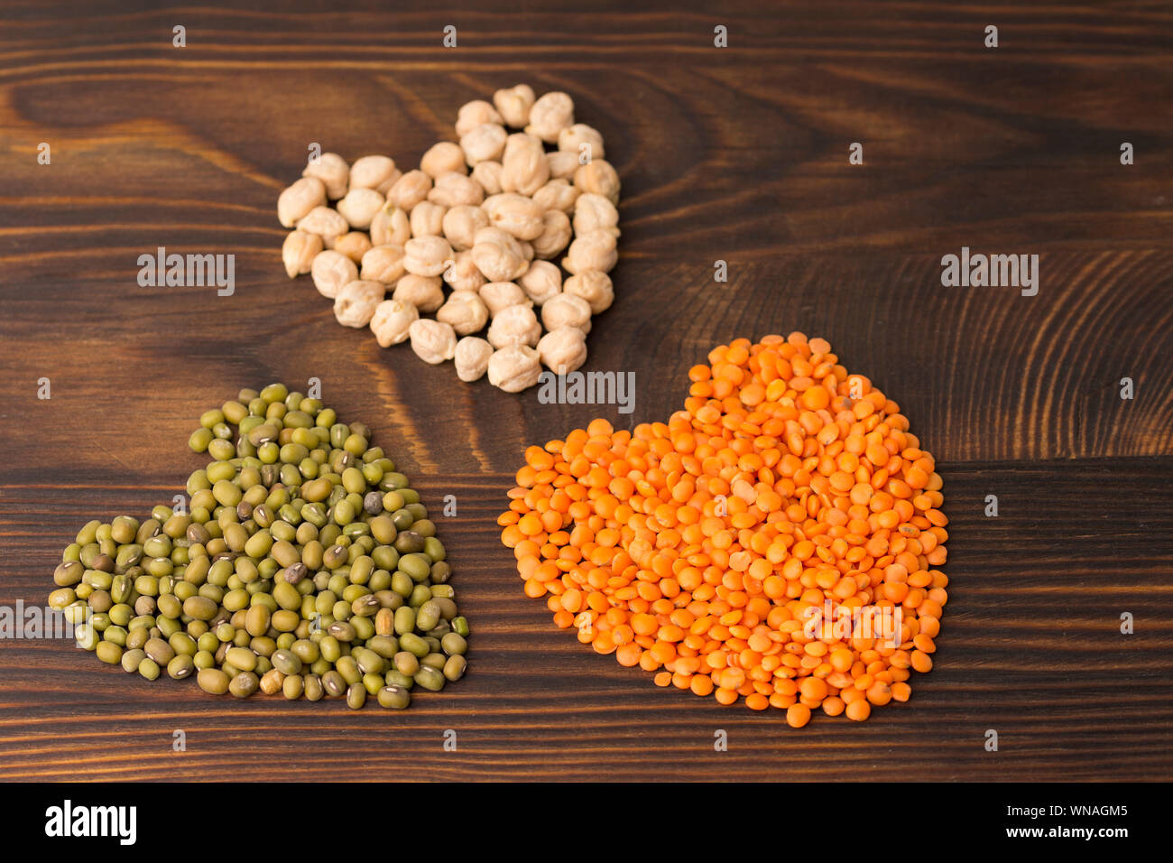 Herzförmige Küken - Erbse, Mung Bohnen und orange Linsen. Holz Hintergrund Stockfoto