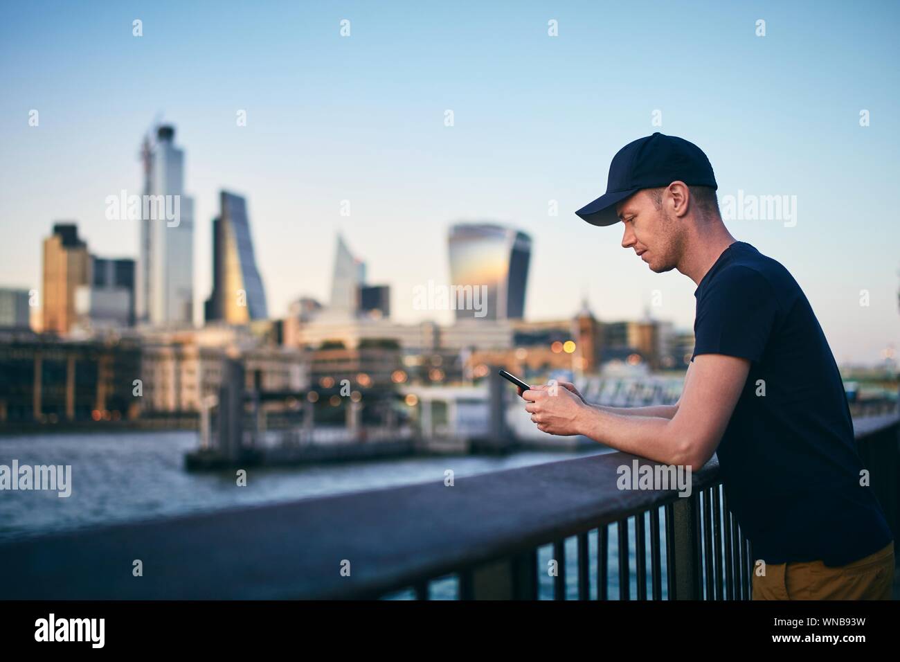 Seitenansicht der junge Mann während der Verwendung von smart phone gegen London Skyline in der Dämmerung. Stockfoto