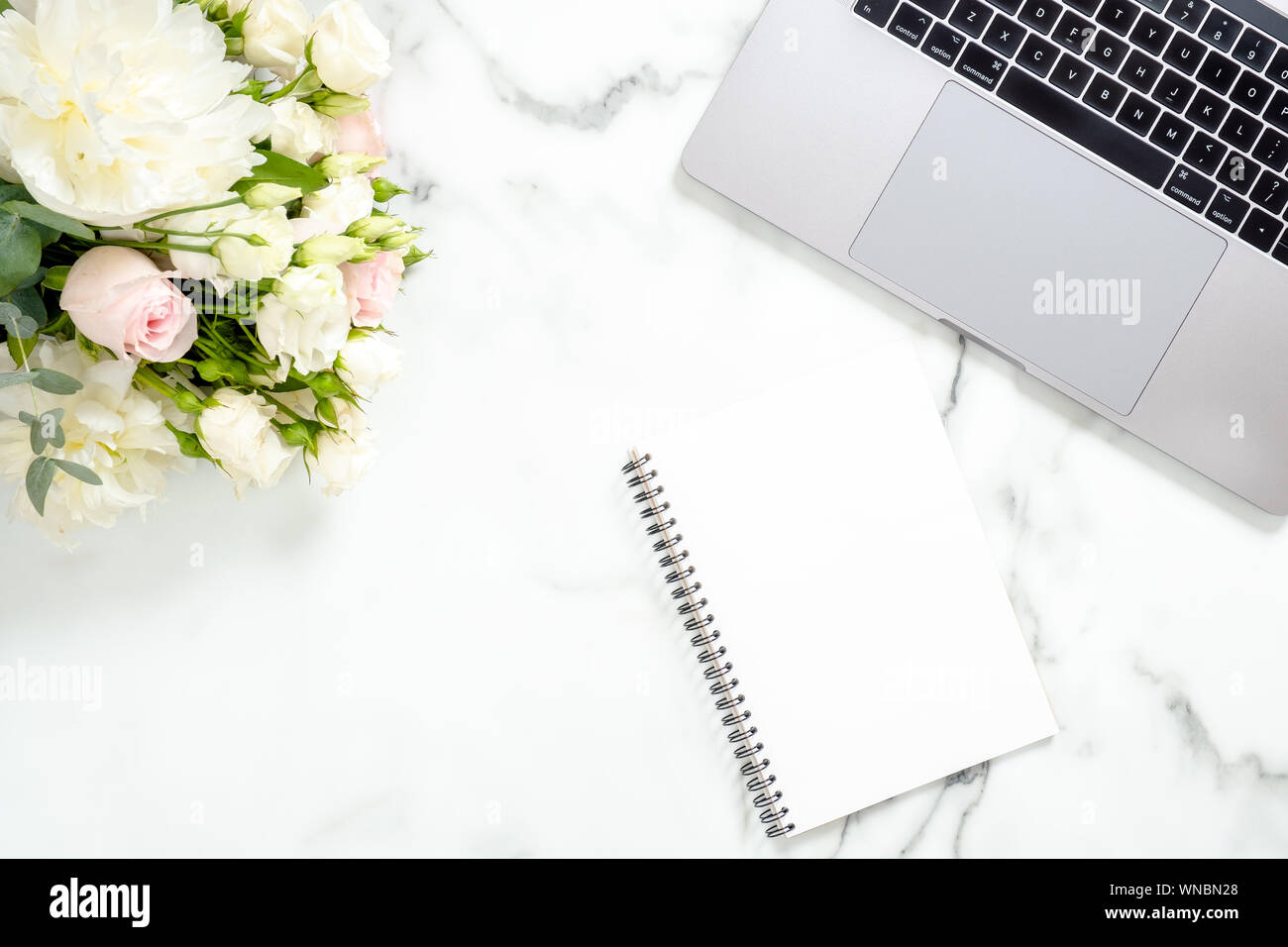 Flach home office Schreibtisch. Weibliche Arbeitsbereich mit Laptop, Blumen, Papier notepad auf weißem Marmor Oberfläche. Ansicht von oben feminin Hintergrund. Busine Stockfoto