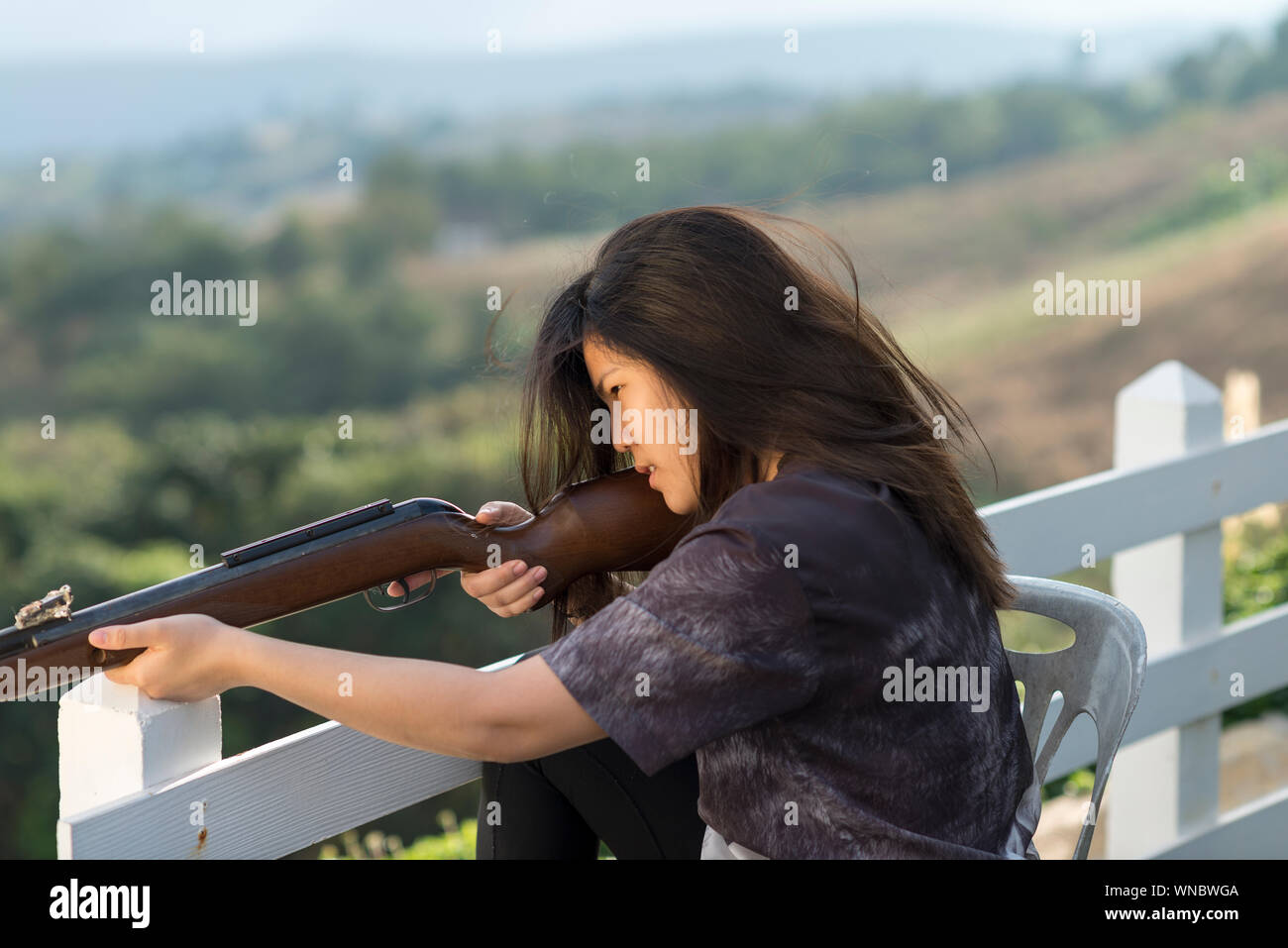 Konzentrierte sich Frau Ziel Gewehr Sitzend auf Stuhl von Geländer über Berg Stockfoto