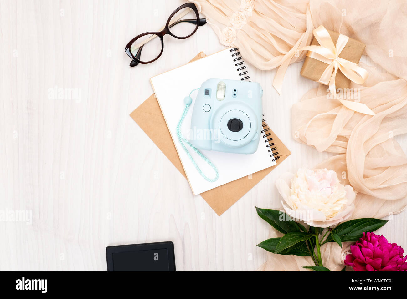 Fashion Blogger home office Schreibtisch mit Frau Artikel: Moderne instant Foto Kamera, Papier notepad, beige Schal, Pfingstrosen Blumen, e-book, Gläser. Top vie Stockfoto