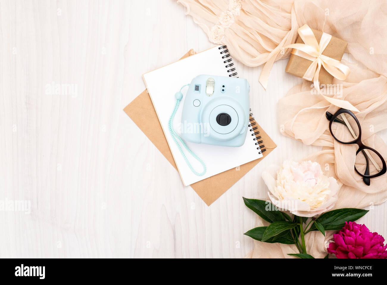 Fashion Blogger home office Schreibtisch mit Frau Artikel: Moderne instant Foto Kamera, Papier notepad, beige Schal, Pfingstrosen Blumen, Gläser. Ansicht von oben, Tende Stockfoto