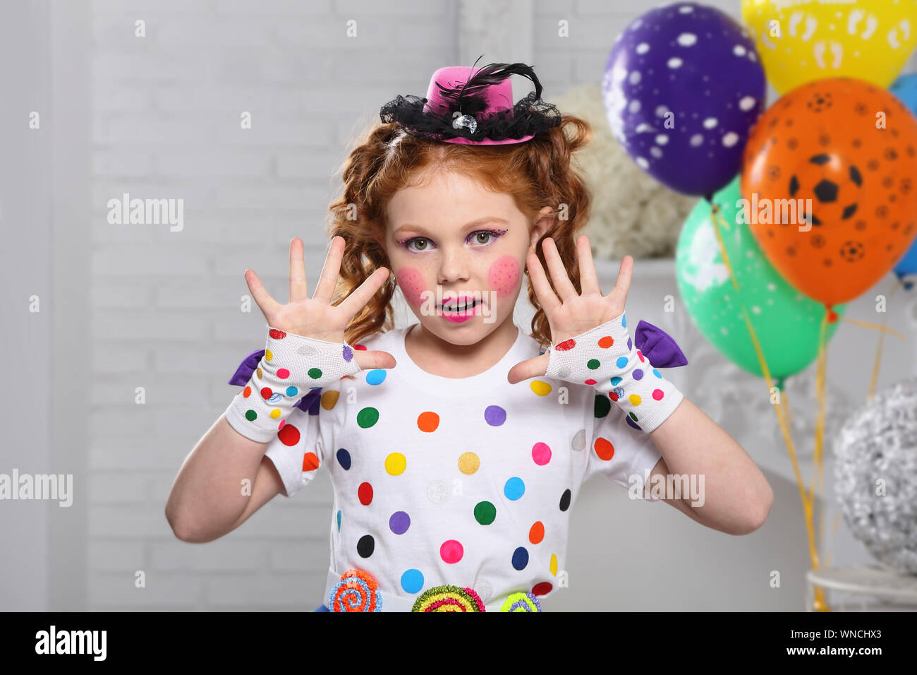 Rothaarige Mädchen im Bild eines Clowns, zeigt seine Hände. . In einem weißen Zimmer mit Luftballons. Stockfoto