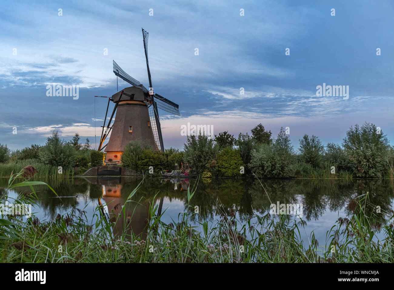 Holländische Windmühle auf dem ruhigen Kanalwasser in den frühen Sonnenuntergang leuchten wider Stockfoto