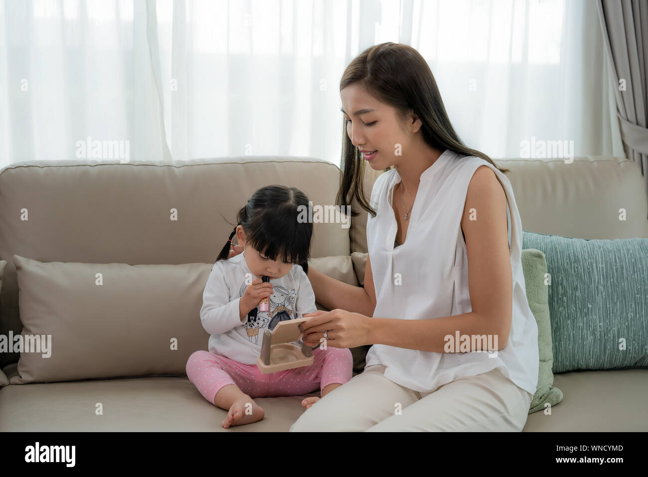 Gerne Asiatische junge Mutter und Tochter in Weiß mit Spaß dabei Lippen-Make-up zu Hause. Stockfoto