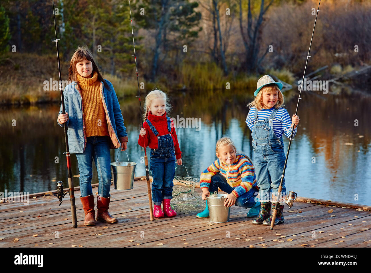 Vier kleine Mädchen fangen Fische auf einem Ponton aus Holz. Angeln mit Freunden. Stockfoto