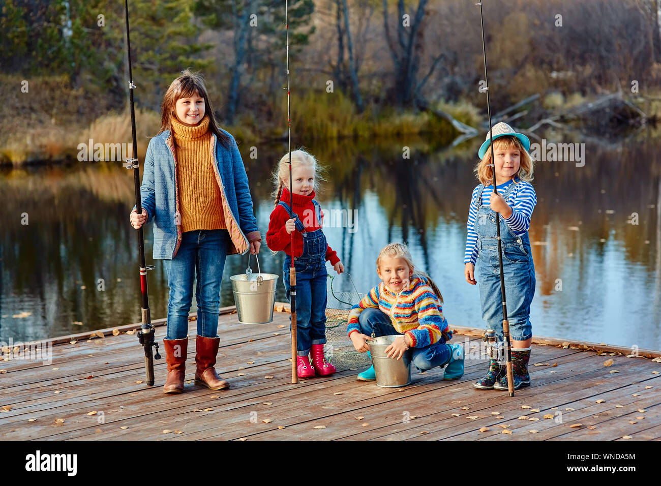 Vier kleine Mädchen fangen Fische auf einem Ponton aus Holz. Angeln mit Freunden. Stockfoto