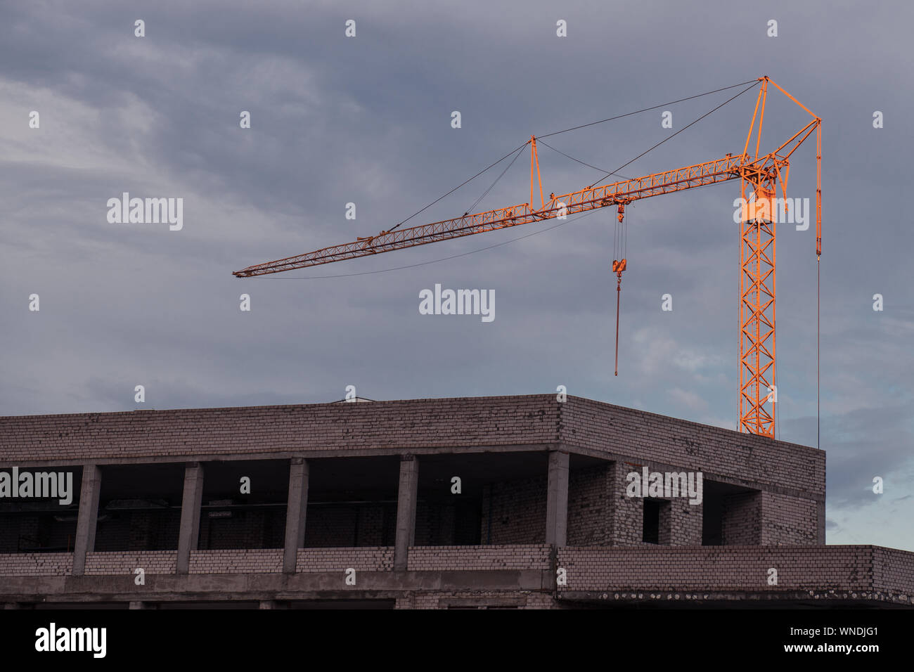 Gebäude im Bau gegen Abend bewölkten Himmel. Big Orange Kran an der Spitze bei der Arbeit. Ansicht von unten. Sonnenuntergang. Stockfoto