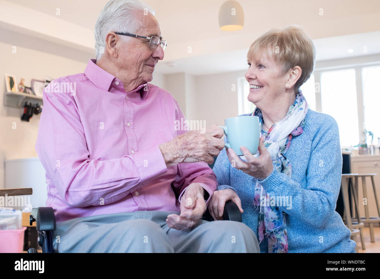 Ältere Frau Übergabe Mann im Rollstuhl heißen Getränk zu Hause Stockfoto